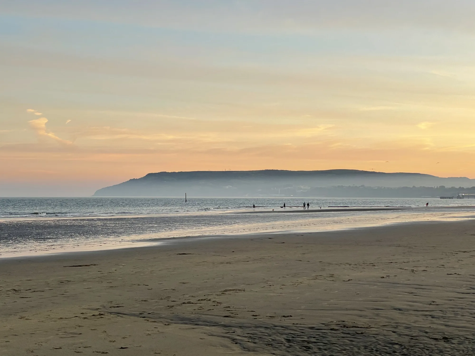 Golden evening light over the wide sands of Sandown Bay at low tide, with walkers at the water's edge